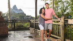 A man and a woman hug against a railing with Expedition Everest Legend of the Forbidden Mountain the background