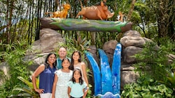 A family pose for a picture outside in front of a statue of Simba, Timon and Pumbaa
