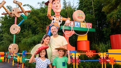 Two kids in cowboy hats and their parents pose for a picture in front of a statue of Woody at the entrance to Toy Story Land