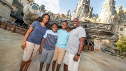 A mom, a dad and their 2 sons pose in front of the Millennium Falcon