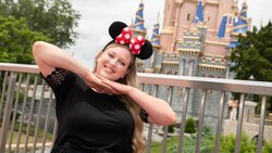 A woman in a wheelchair smiles for the camera on Fantasyland Bridge near Cinderella Castle