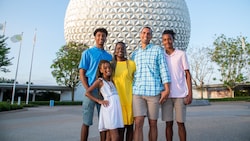 A family smiles and poses in front of Spaceship Earth at EPCOT