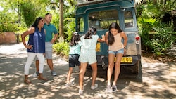 Three children pretending to push a Kilimanjaro Safaris vehicle as their parents look on and laugh