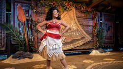 Moana poses in front of an island-themed mural shaped like a sail