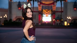 A woman wears a Minnie Mouse headband near Mickey and Minnie's Runaway Railway