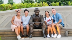 A family of 4 sitting on a bench with a statue of Walt Disney
