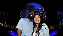 A couple poses and smiles in front of the Spaceship Earth attraction at Epcot