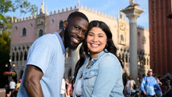 A couple smiles and poses for a picture in front of the Italy Pavilion at Epcot