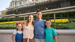 A family of 4 posing in front of the Main Street, U.S.A. train station at Magic Kingdom park