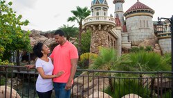 A man and woman gazing at one another as they stand on a bridge near Prince Eric’s castle at Magic Kingdom park