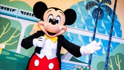 Mickey Mouse in a tuxedo posing in front of a backdrop featuring the monorail and Spaceship Earth at Epcot