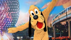 Pluto posing in front of a backdrop featuring Spaceship Earth and the monorail at Epcot