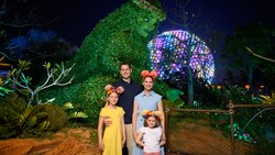 A family of 4 posing in front of the Te Fiti topiary with Spaceship Earth in the background at Epcot 