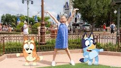 En un Disney Magic Shot, Bingo y Bluey de la serie Bluey aparecen junto a una niña sonriente de pie frente a Cinderella Castle en Walt Disney World Resort