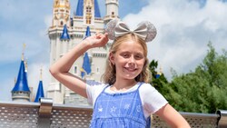 A smiling girl wearing a Minnie Mouse ear headband strikes a pose in front of Cinderella Castle at Walt Disney World Resort