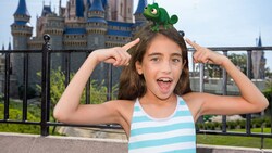 A Disney Magic Shot, featuring Pascal from the movie Tangled, as it sits atop the head of a girl standing in front of Cinderella Castle