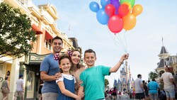 A family of 4 poses for a Magic Shot featuring balloons along Main Street, U S A