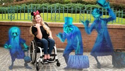 A woman in a wheelchair takes a photo in the Haunted Mansion courtyard with images of the Hitchhiking Ghosts