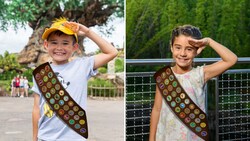 A boy and girl giving a salute dressed as Wilderness Explorers, wearing sashes covered in badges, at Disney’s Animal Kingdom theme park