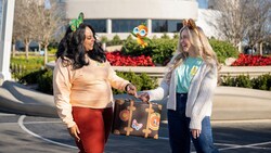 Two Guests wearing Minnie Mouse ear headbands, holding a suitcase together and posing with a Disney Photopass Magic Shot overlay of Orange Bird