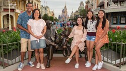 A family of 5 pose with a statue of Roy Disney and Minnie Mouse