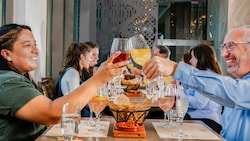 A smiling couple clinking their glasses across a table before taking a sip from their beverages