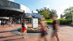 Guests walking past the Test Track entrance sign at Epcot as the monorail passes
