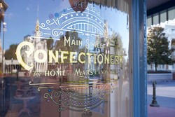 A storefront window with a logo that says, 'Main Street Confectionery, the Home of Mars Candy Treats'