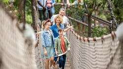 A family of 4 walking across a wooden plank and rope bridge at Pirate’s Lair on Tom Sawyer Island