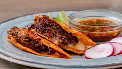 Dos Tacos Quesa Birria en un plato con rodajas de rábano y un tazón de salsa