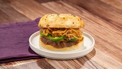 Un hamburger de bœuf avec une sauce au fromage jalapeño, des oignons croustillants et d’autres ingrédients sur un pain aux oignons