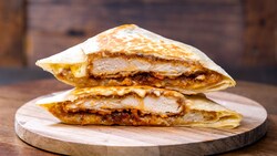 Both halves of a folded chicken sandwich with melted cheese served on a round wooden board