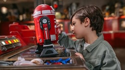 A young boy examining an assembled droid resting on a workbench at Droid Depot