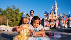 Two young girls in Disney Princess dresses strike a pose in front of Sleeping Beauty Castle at Disneyland Park