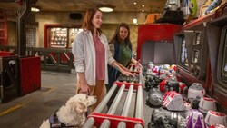 Una mujer lee las instrucciones en braille para construir un droide en la tienda de droides, mientras una chica Miembro del Elenco la observa.