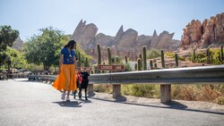 Una mujer y su perro de servicio caminan por Radiator Springs Racers, con las montañas Cadillac Range en el fondo.