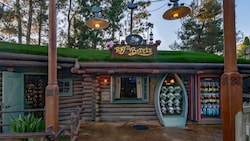 A cabin with grass on the roof, merchandise displayed out front and a sign that says ‘Ray’s Berets’