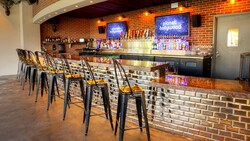 O Stargazers Bar no Disney Springs com um bar com tampo de granito, banquetas, detalhes em tijolos à mostra e prateleiras com garrafas de bebidas alcoólicas