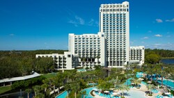 A large hotel featuring a winding pool lined with reclining beach chairs and palm trees