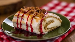 An ice cream cake roll covered in meringue with a crumble topping and ribbons of cherry glaze