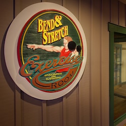 A sign saying ‘Bend and Stretch Exercise Room’ hanging on a wall next to a fitness center