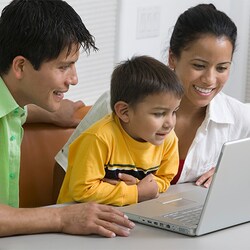 A smiling mother, father and young son looking at the screen of an open laptop computer