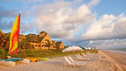 A beach with lounge chairs, umbrellas and rental boats, with the Resort behind