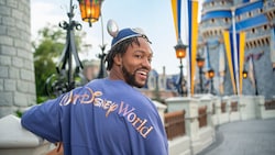 A man standing near Cinderella Castle, wearing a Mickey Mouse ear hat and a shirt with the words ‘Walt Disney World’ on the back,