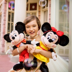 A young girl holding a plush Minnie Mouse and plush Mickey Mouse, standing outside in Magic Kingdom park 