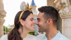 A man wearing a button down shirt featuring Cinderella Castle, cozying up to a woman wearing a Minnie Mouse ear headband 