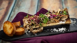 A piece of bone marrow topped with mushrooms and micro greens, served with slices of bread