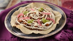 A large tostada topped with ground chorizo, bean puree, salsa verde and red onions