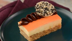 A slice of cake topped with orange ganache and a sesame tuille