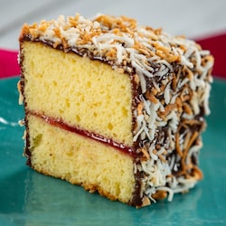 A slice of lamington, featuring yellow cake with a raspberry filling, covered in chocolate and coconut